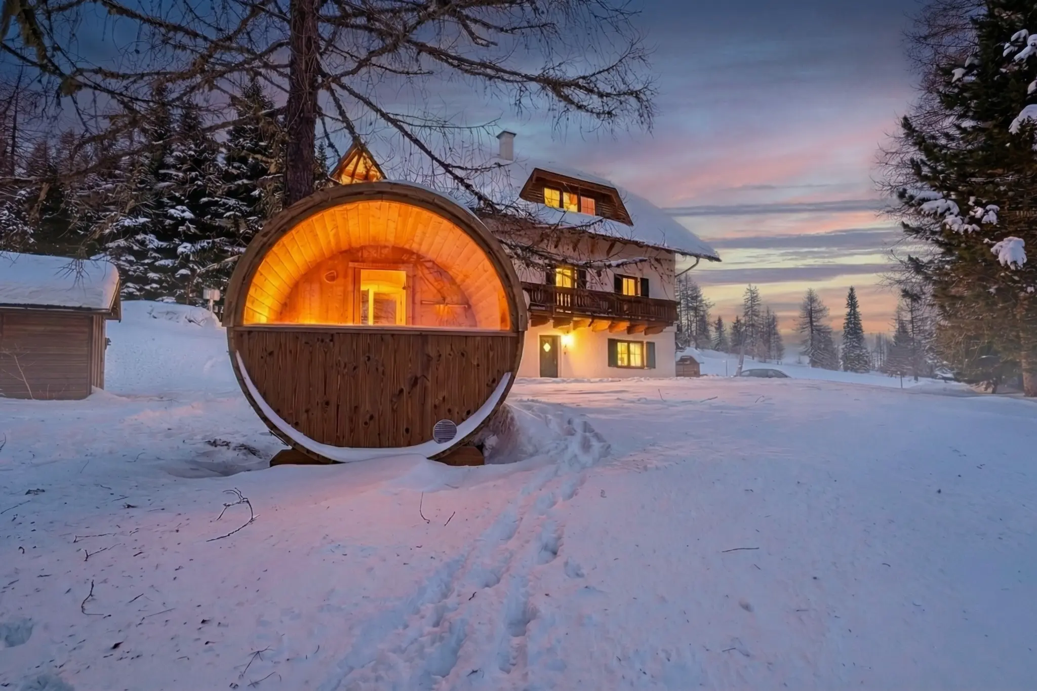 Berglodge Hochrindl mit privater Fasssauna im Schnee bei Abenddämmerung